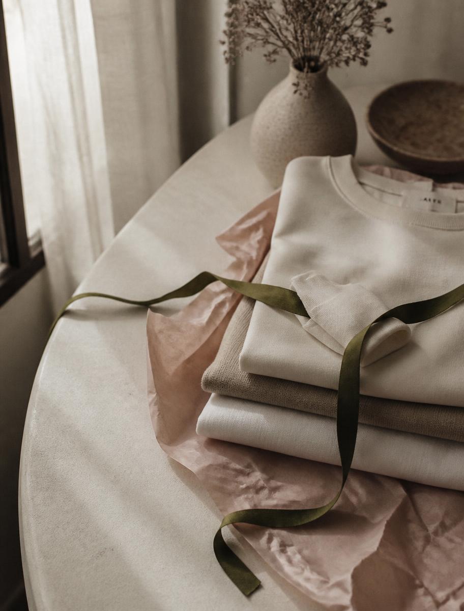 Prendas dobladas sobre papel de seda rosa con una cinta verde oliva